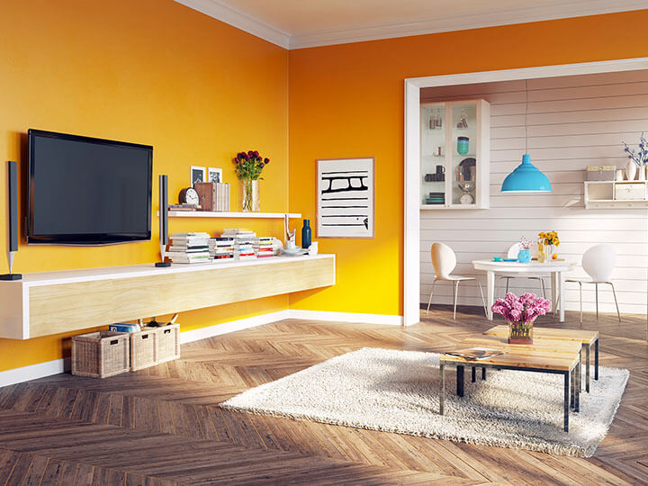 Sala de estar com uma parede amarela vibrante, com uma TV montada e prateleiras com livros.